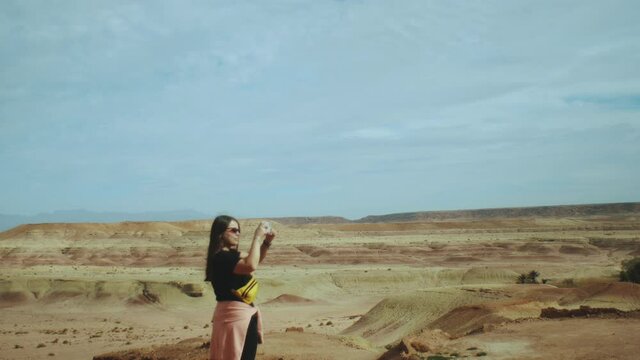  Woman in sunglasses staying on the rocky hills and taking pictures of beautiful desert hills landscape in Morocco, 4k