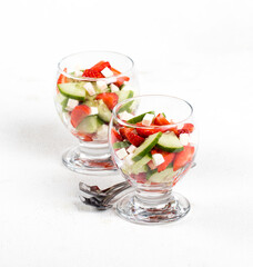 Berry and vegetable salad of strawberries and cucumber with feta cheese in a glass on a light...