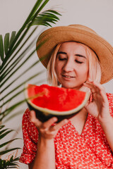 Young beautiful lady in red dress and straw hat is holding juicy watermelon. Red bright color. Green tropical. Summer time vacation. Beach vibes. Hot days. Refreshing red fruit.Pretty millennial woman