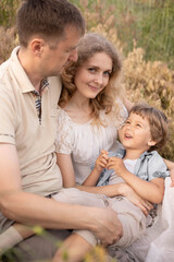 Happy family, cuddling in the field, mom and dad love their son, baby with golden hair, blonde woman, beautiful people, games with parents, bright children