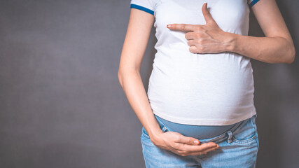 Pregnant woman holds hands on belly on a gray background. Copy space, pregnancy, motherhood, people and expectation concept. Close-up, copy space, indoors. Toned photo of pregnancy.