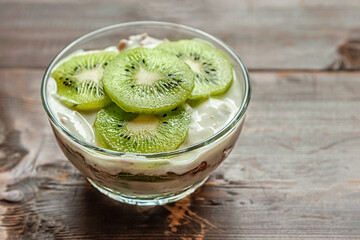 Naklejka na ściany i meble homemade delicious layered dessert of yogurt, muesli and kiwi fruit on a wooden table