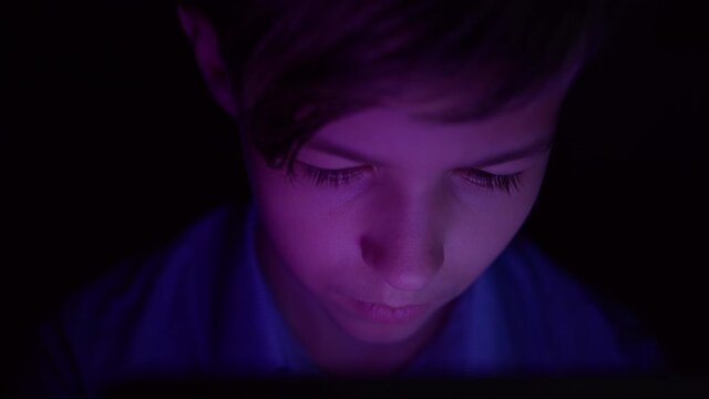 Portrait of a serious boy looking at tablet in dark night, Thoughtfully doing some action at night on the tablet
