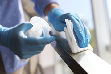 Woman in latex gloves cleaning railing with wet wipe and detergent indoors, closeup