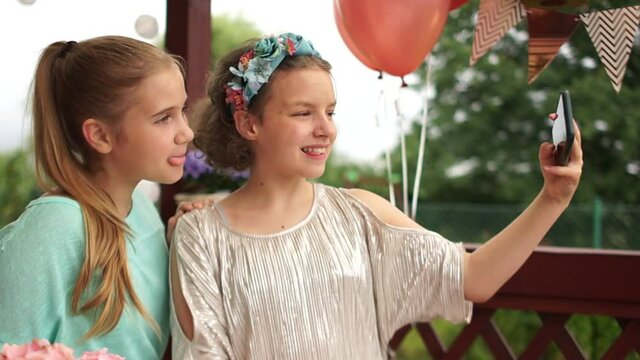 Two teen girl friends take a selfie during a birthday party. Childrens holiday, elegant beautiful girls are photographed together, outdoor portrait