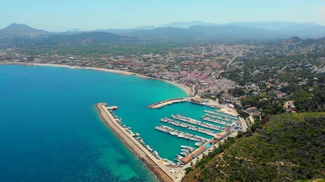 Aerial drone point of view coastal town of Javea with green mountains, turquoise bay Mediterranean Sea moored vessels in harbour, comarca of Marina Alta in province of Alicante, Valencia, Spain