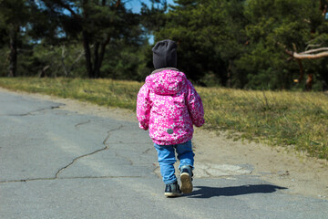 Little lonely child in a bright pink jacket turned back walks outdoors