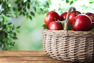 Juicy red apples in wicker basket on wooden table outdoors. Space for text