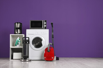 Set of different home appliances with vacuum cleaner on purple background indoors. Space for text