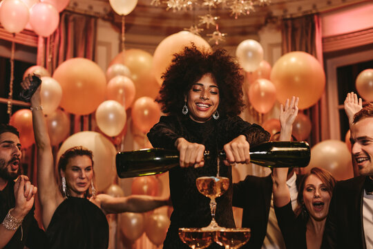 Woman filling champagne pyramid with friends dancing at party