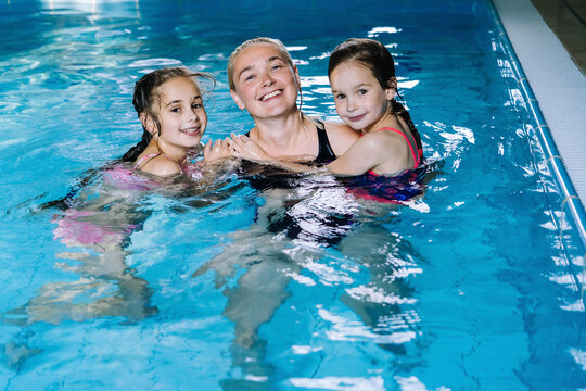 Mother with two daughters having fun in indoor swimming-pool. Girl is resting at the water park. Swimming school for small children. Concept friendly family sport summer vacation. Selective focus