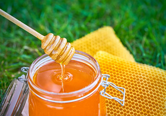 Open jar of fresh honey and honeycombs on the grass, sunlight. Top view.