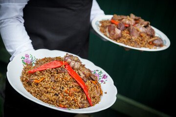 A hand holds the national dish of Uzbek pilaf with vegetables.