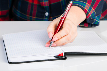 Left-handers Day. Business woman writes a note in notebook. Girl holds a pen in her left hand close-up.