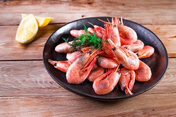 Appetizing boiled shrimp on a skewer in a black plate on a wooden surface among lemon. The concept of fast and wholesome food