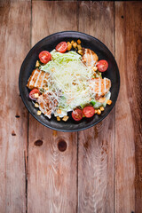 Appetizing Caesar salad with chicken in a black plate on a wooden table. The concept of healthy food and serving