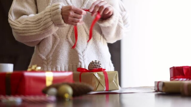Woman in sweater is wrapping a Christmas gift on a table