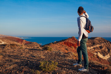 Hiker walking by White beach on Santorini island Greece enjoying sea mountain landscape. Man backpacker traveling