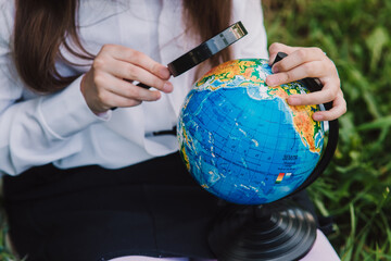 Back to school. Happy schoolgirl are viewing the globe. Girl examines the globe with ukrainian signature under a magnifying glass. Soft focus