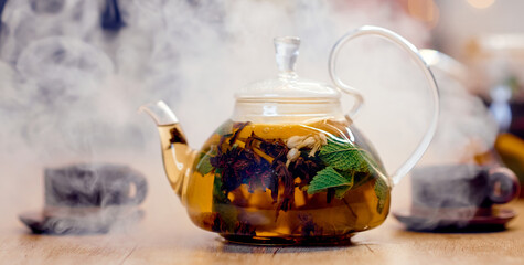 beautiful transparent teapot with colorful tea inside two cups in the background