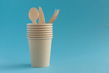Fototapeta na wymiar Eco-friendly disposable paper cups and cutlery made of wood spoons, forks and knives on a blue background. Ecology, concept of zero waste. Place for text