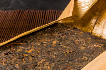 Chinese pressed PU-erh tea in bamboo leaf packaging on a bamboo Mat, close-up, macro