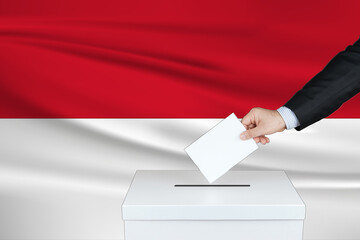 Election in Indonesia. The hand of man putting his vote in the ballot box. Waved Indonesia flag on background.                  