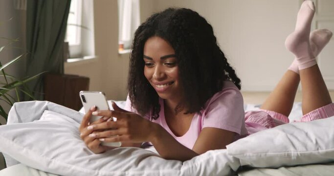 Black girl chatting with friends on cellphone, lying in bed