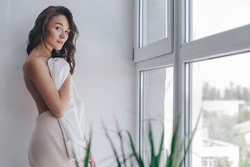 beautiful topless girl covered up with a jacket and stands near the window