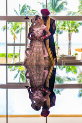 Sikh bride and groom wearing bright traditional clothing on clear sandy beach beneath sunny blue skies