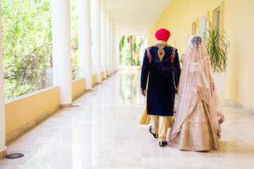 Sikh bride and groom wearing bright traditional clothing on clear sandy beach beneath sunny blue skies