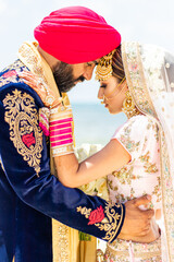 Sikh bride and groom wearing bright traditional clothing on clear sandy beach beneath sunny blue skies