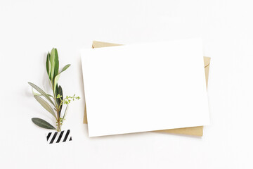 Feminine stationery, desktop mock-up scene. Blank horizontal greeting card, craft envelope and washi tape with green olive branch.White table background. Flat lay, top view. No people. © tabitazn