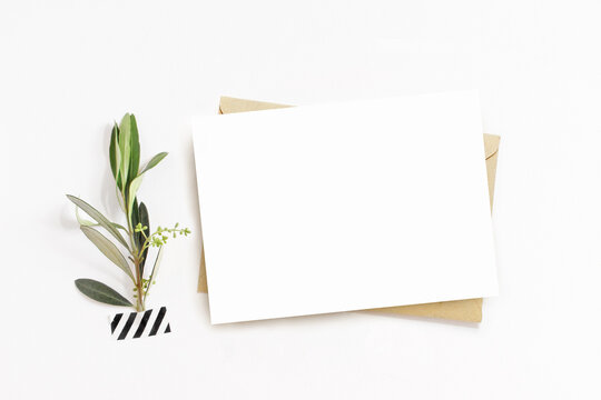 Feminine Stationery, Desktop Mock-up Scene. Blank Horizontal Greeting Card, Craft Envelope And Washi Tape With Green Olive Branch.White Table Background. Flat Lay, Top View. No People.