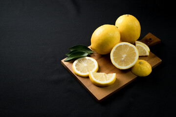 Fresh yellow lemon lime fruit with slices and fresh lemon juice on wood cutting board on black background , Copyspace for text.