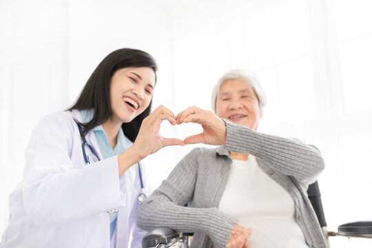 asian female doctor and old patient show heart sign with hand, happiness and relationship in hospital, they feeling happy and smile on white background
