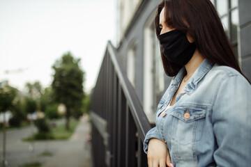 girl in a protective mask on a balcony looks at an empty city