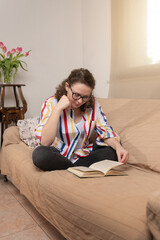Obraz premium Focused adult woman reading book on couch at home, stay at home concept