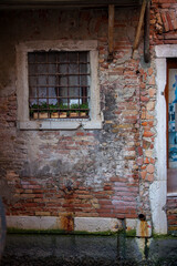 A small window with bars inset into old bricks by a door to an apartment on a canal in Venice, Italy.