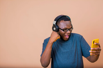 image of a young overexcite black African boy wearing headphone, and holding a mobile phone. Music...