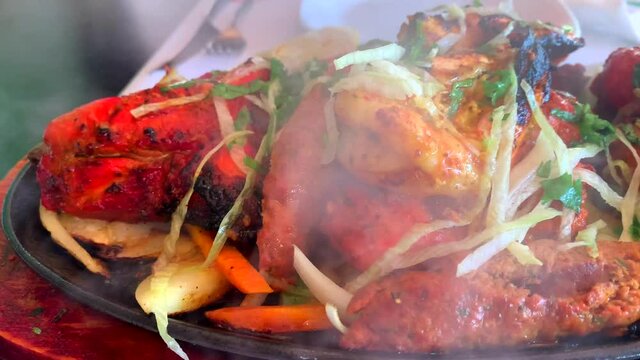 Indian tandoori mixed meat grilled dish, sizzling meats with steam coming off, restaurant food