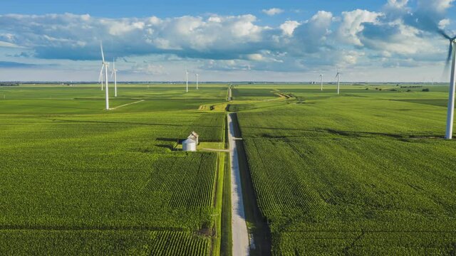 Flying above green corn fields with rural road and wind turbines on the horizon. Hyper lapse, late afternoon light 