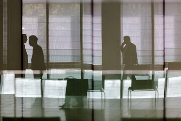 silhouettes of businessmen in building lobby as seen through glass wall at workplace