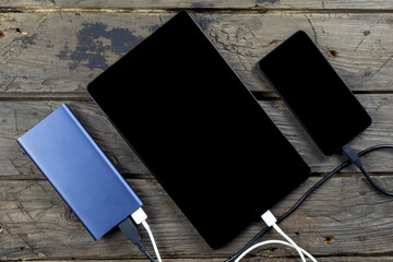 Mobile devices smartphone, tablet and power bank on wooden table. Connect of using charger. Shown use of portable charger.