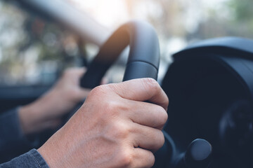 man hand steering the wheel while driving a car on the road