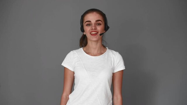 smiling young call center dispatcher woman wearing headset answering customers isolated over grey