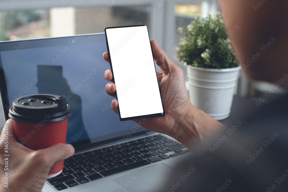 Aufkleber mockup of man using blank screen mobile smart phone and working on laptop computer at home office