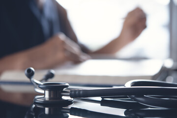 Close up of stethoscope with male doctor reading a book as background