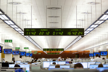 Digital time zone clock hanging over business people working on trading floor