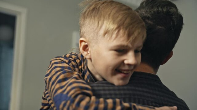 Young Dad Finally Coming Home From Work. Smiling Son Meeting His Dad At The Door In The Evening. Concept Of Joy. Close-up Of Happy Teenage Son In Casual Clothes Runnig To His Father And Hugging Him.